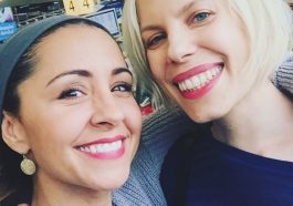 Two women smiling at the camera in a busy indoor setting.