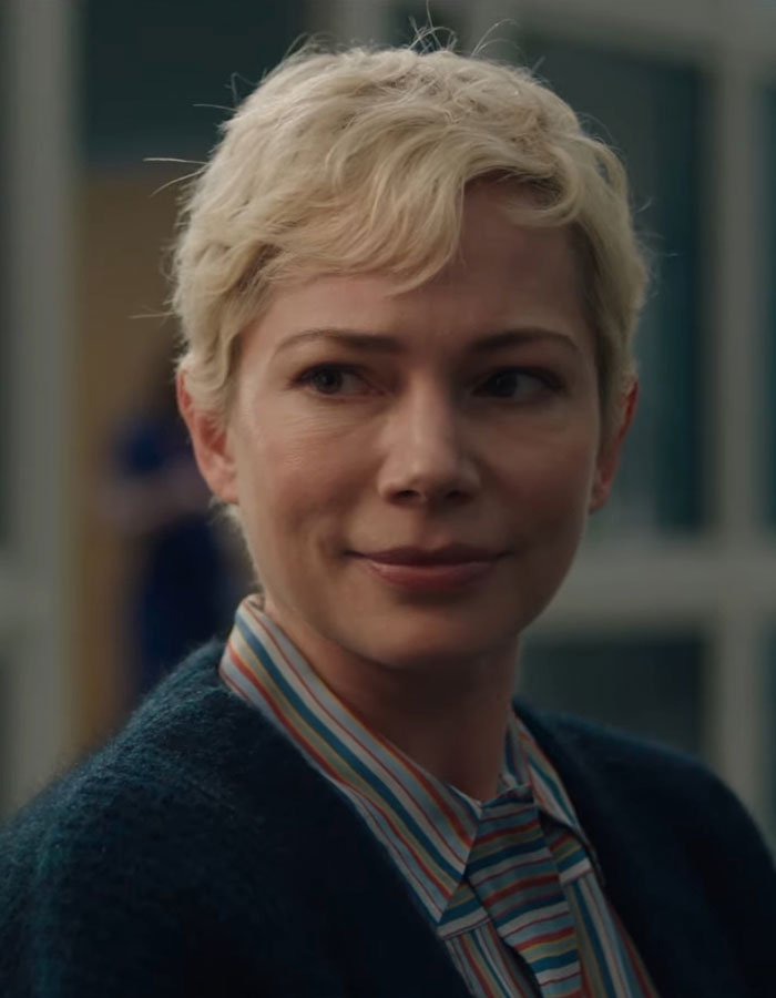 Short-haired woman smiling gently, wearing a striped shirt and dark sweater, indoors.